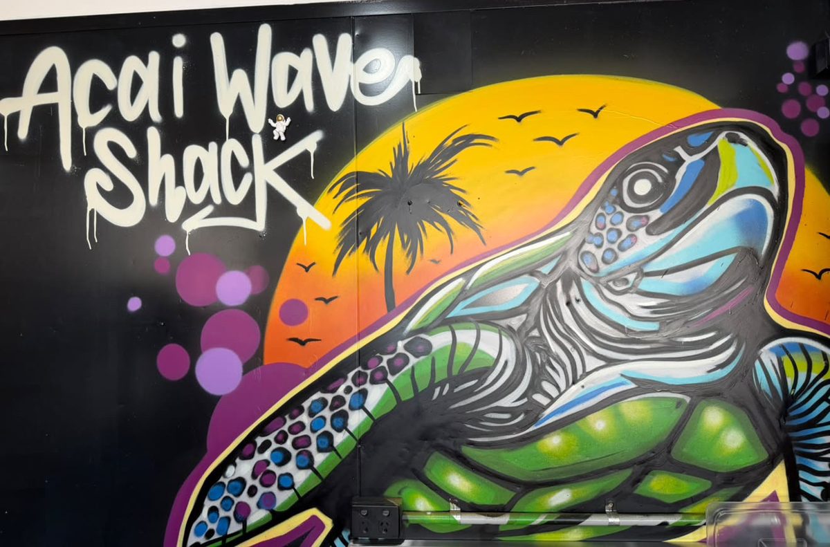 Spray-painted mural inside the shop: a sea turtle in front of a sunset and palm tree beside the words Acai Wave Shack